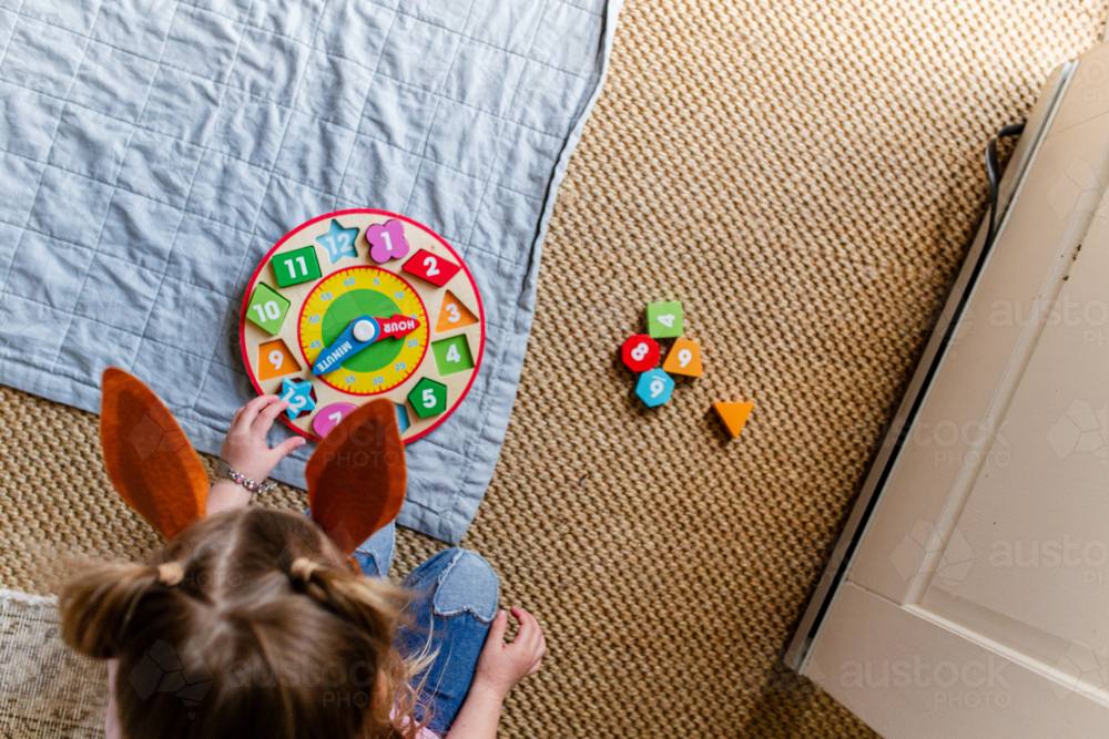 Image of Young girl playing with wooden clock on the floor - Austockphoto