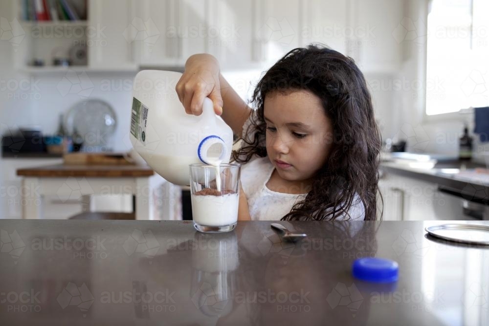 Young girl pouring milk into a glass - Australian Stock Image
