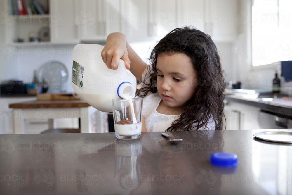 Young girl pouring milk into glass - Australian Stock Image