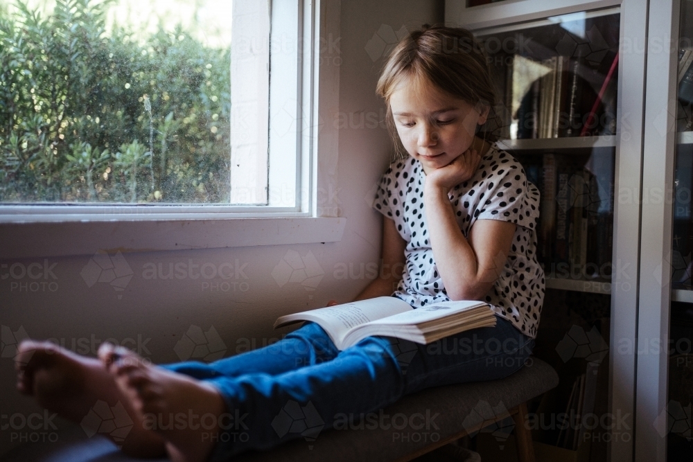Young girl reading a book at home - Australian Stock Image