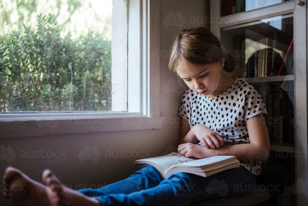 Young girl reading a book at home - Australian Stock Image