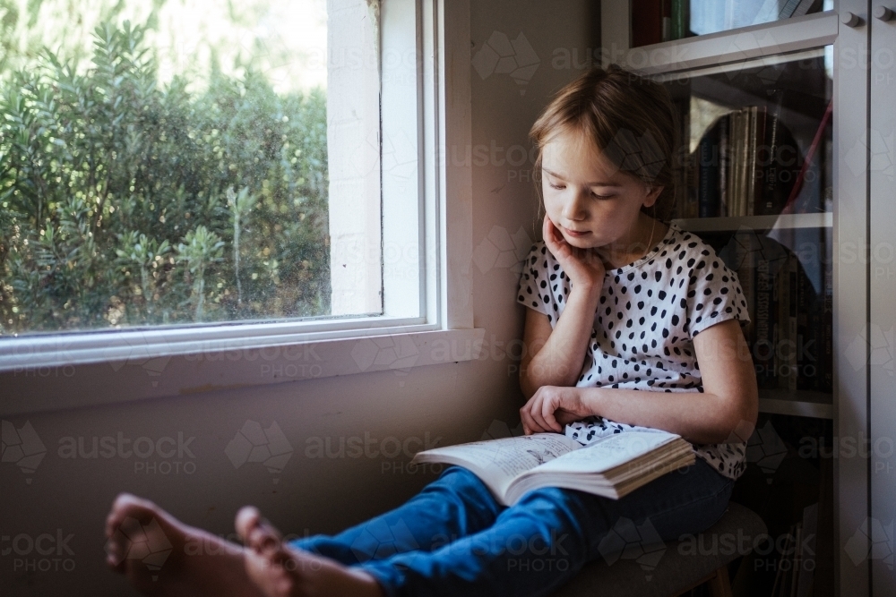 Young girl reading a book at home - Australian Stock Image