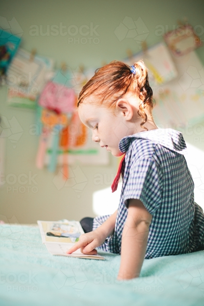 Young girl reading a book in a bedroom - Australian Stock Image