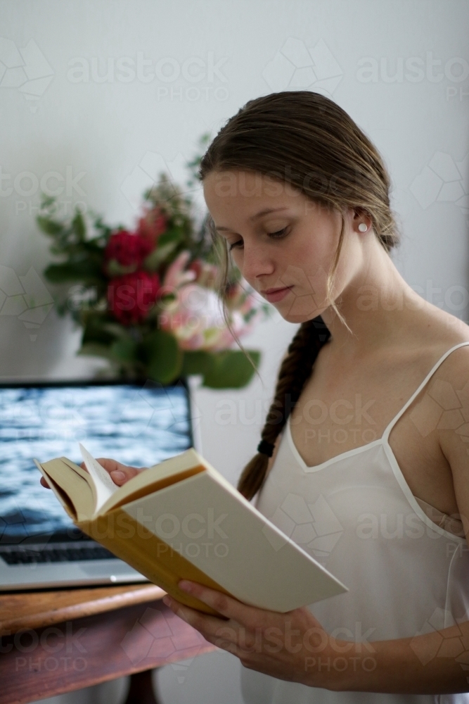 Young girl reading a book indoors by her work desk - Australian Stock Image