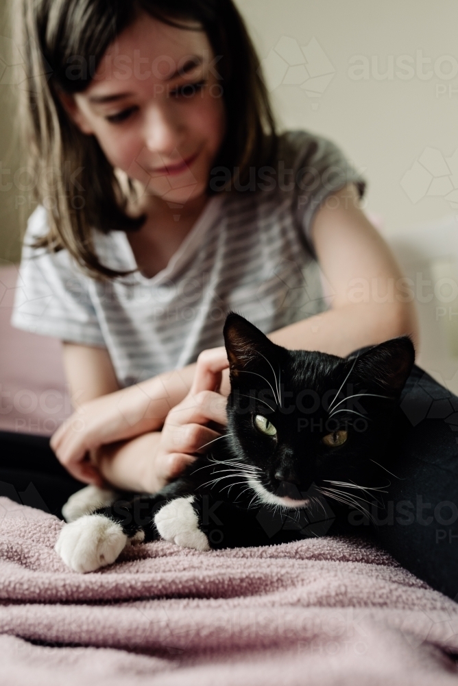 Young girl relaxing with her cat on her bed. - Australian Stock Image