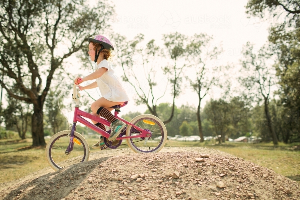 Young girl riding a bike over a hill in backyard - Australian Stock Image