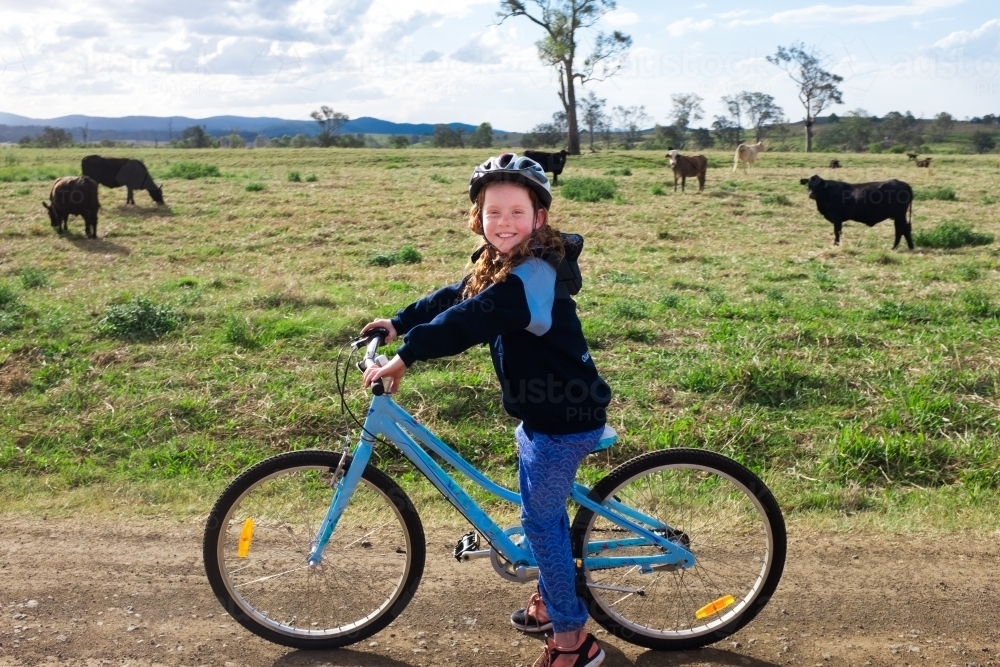 Young girl riding a bike through a cow paddock - Australian Stock Image