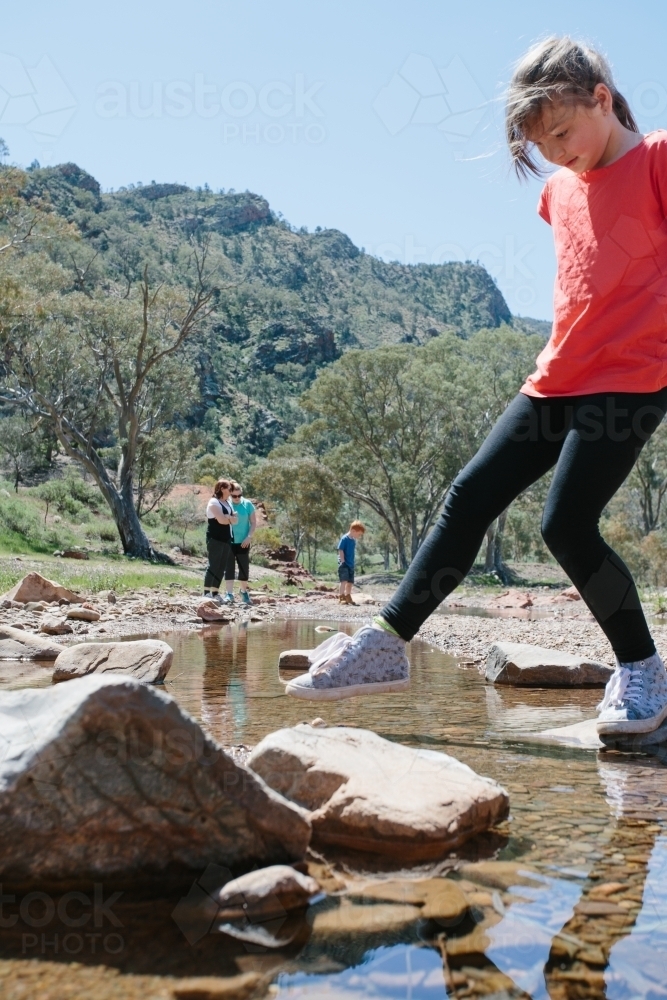 Young girl rock hopping through a creek during a bush walk - Australian Stock Image