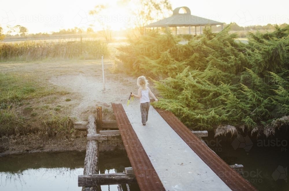 Young girl running over bridge at sunset - Australian Stock Image