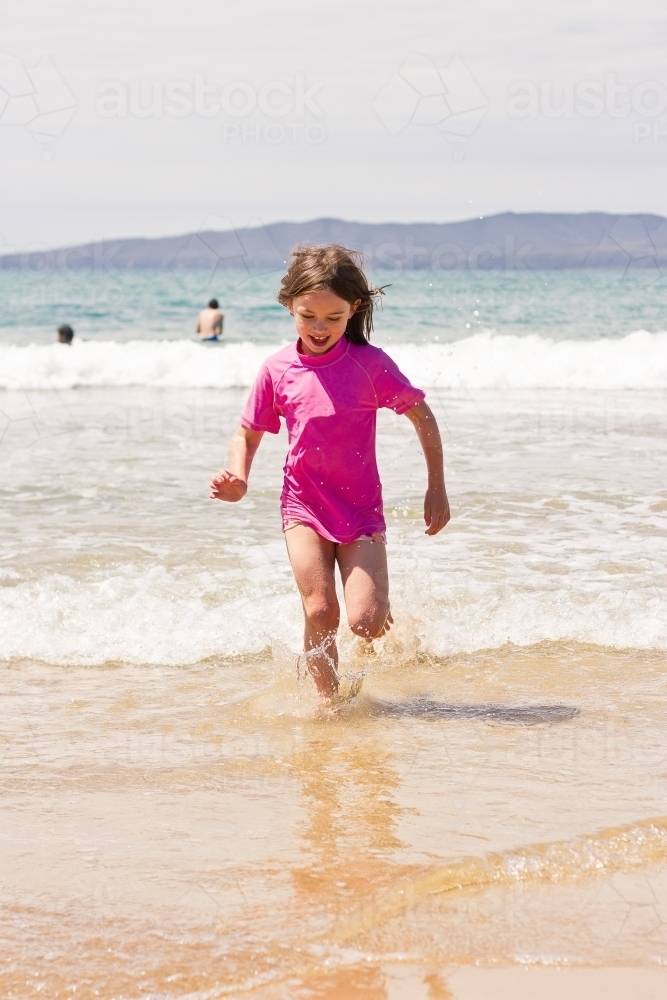 Young girl running through waves at the beach - Australian Stock Image