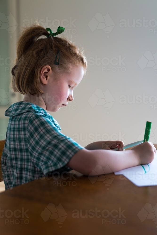 Young girl sitting at a desk drawing and writing - Australian Stock Image