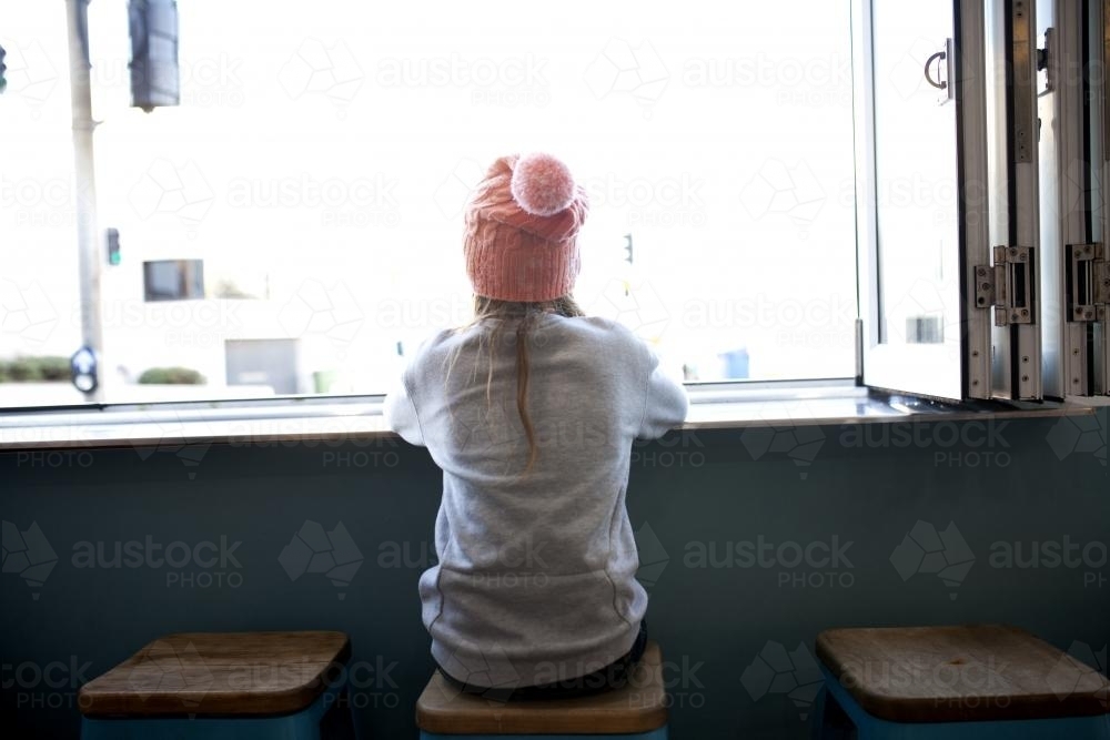 Young girl sitting in a cafe window looking out - Australian Stock Image