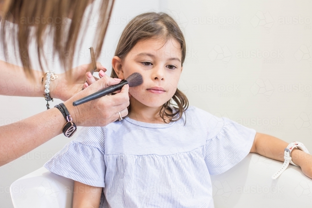 Young girl sitting in chair getting makeup done - Australian Stock Image