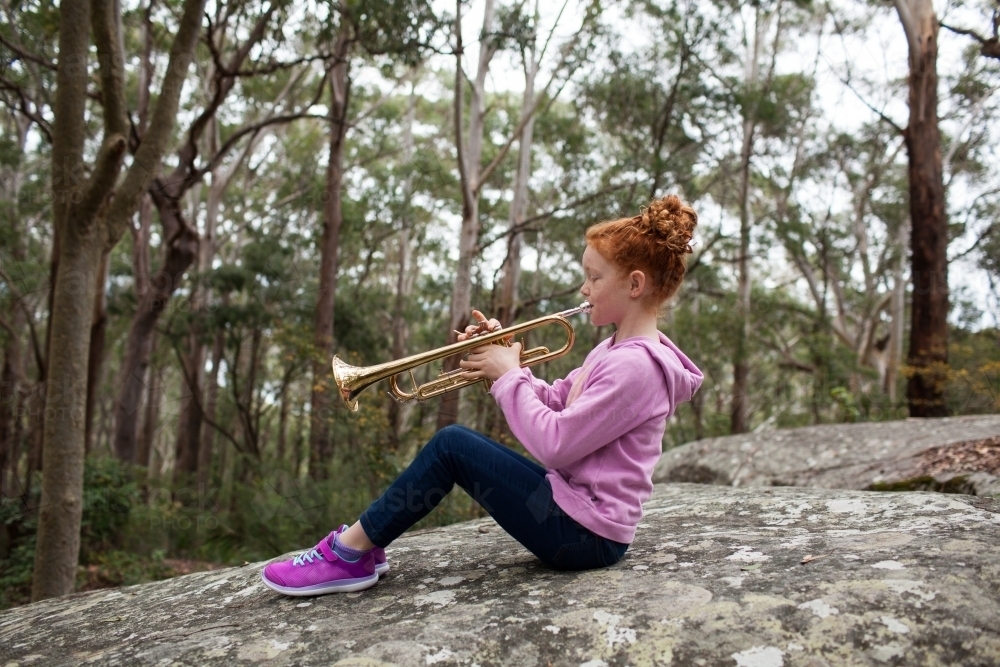 Young girl sitting on a rock playing a trumpet - Australian Stock Image