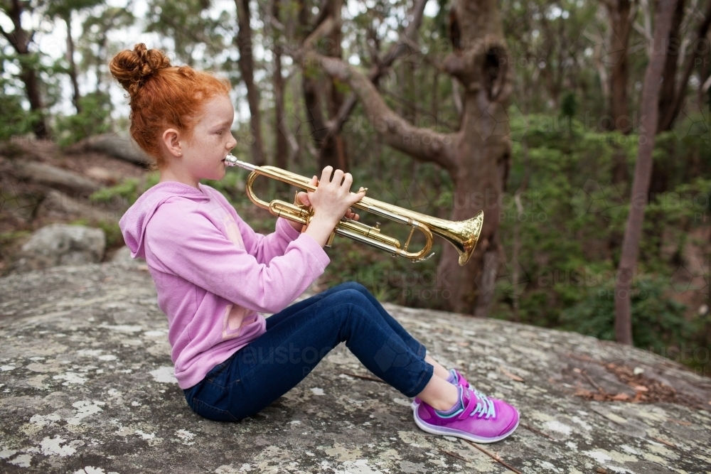 Young girl sitting on a rock playing a trumpet - Australian Stock Image