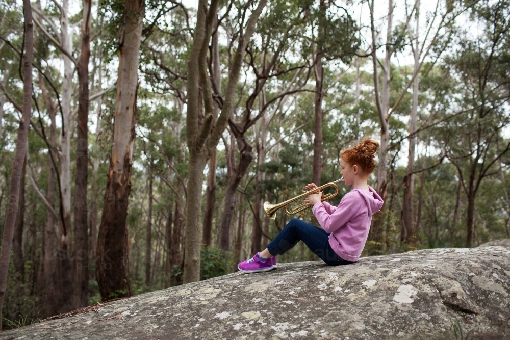 Young girl sitting on a rock playing a trumpet - Australian Stock Image