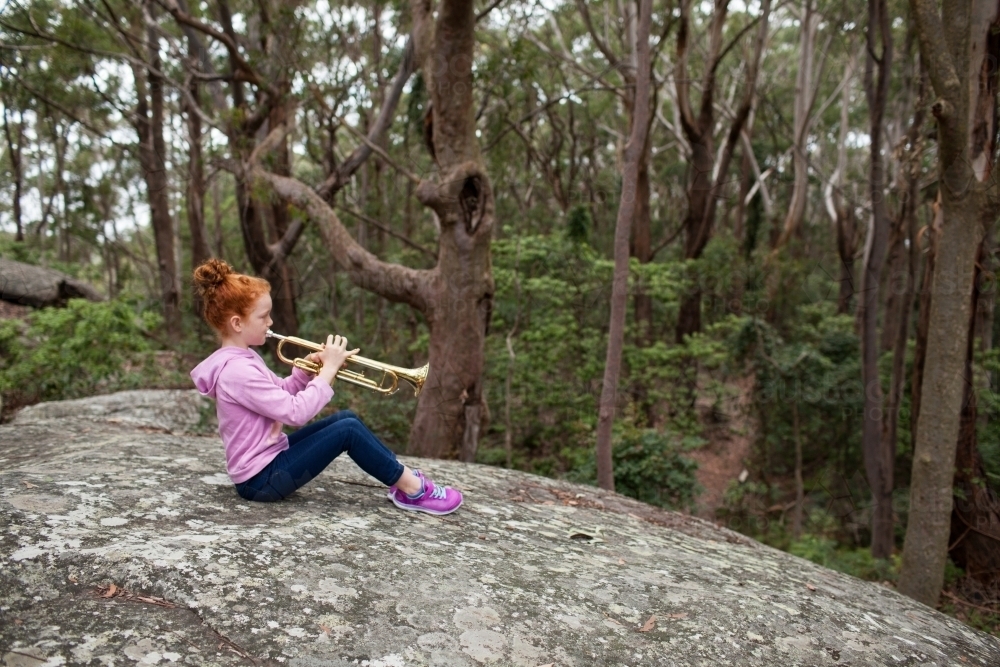 Young girl sitting on a rock playing a trumpet - Australian Stock Image