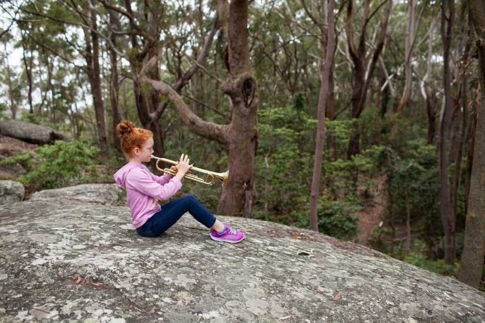 Young girl sitting on a rock playing a trumpet - Australian Stock Image