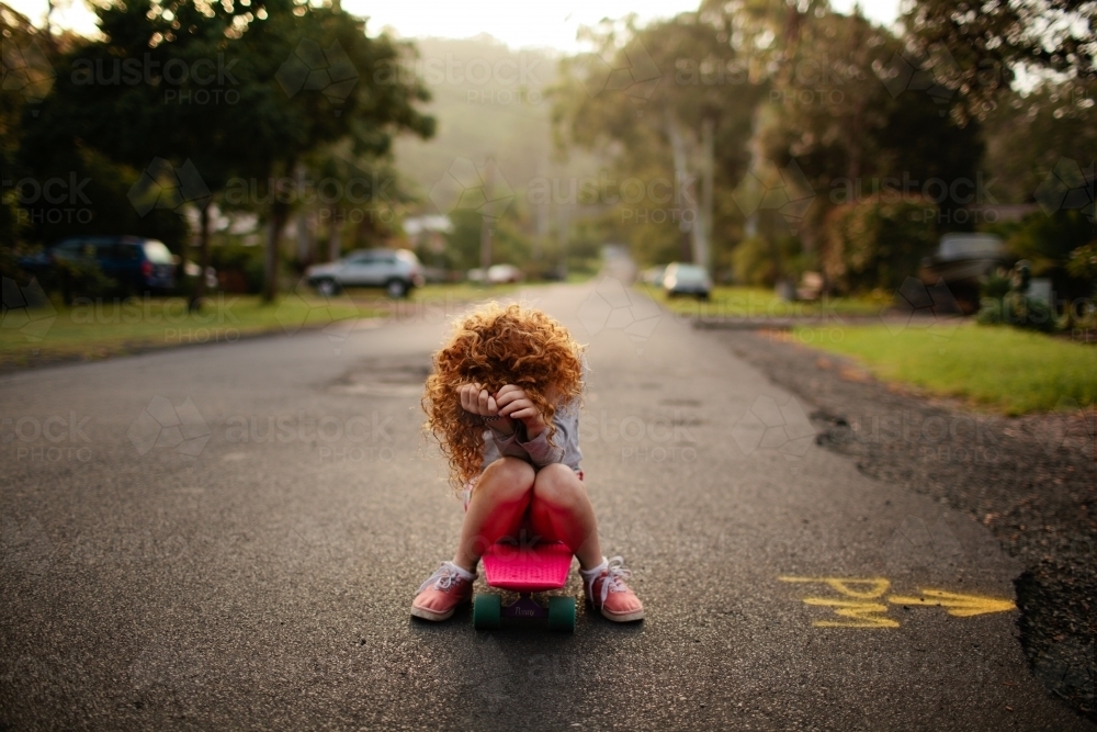 Young girl sitting on a skateboard on a road - Australian Stock Image