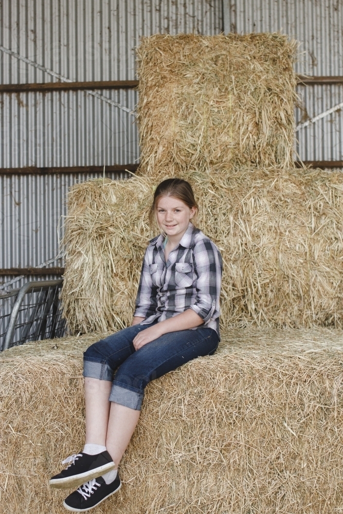 Young girl sitting on a stack of hay bales - Australian Stock Image