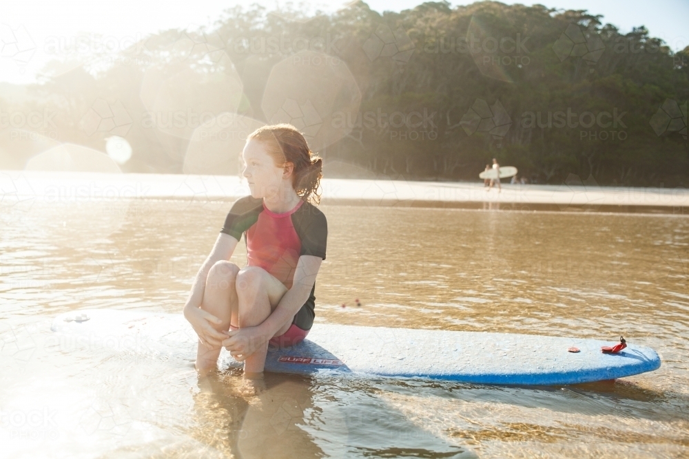 Young girl sitting on a surfboard at the beach - Australian Stock Image