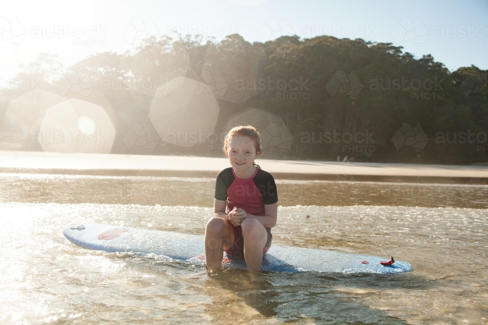 Young girl sitting on a surfboard at the beach - Australian Stock Image