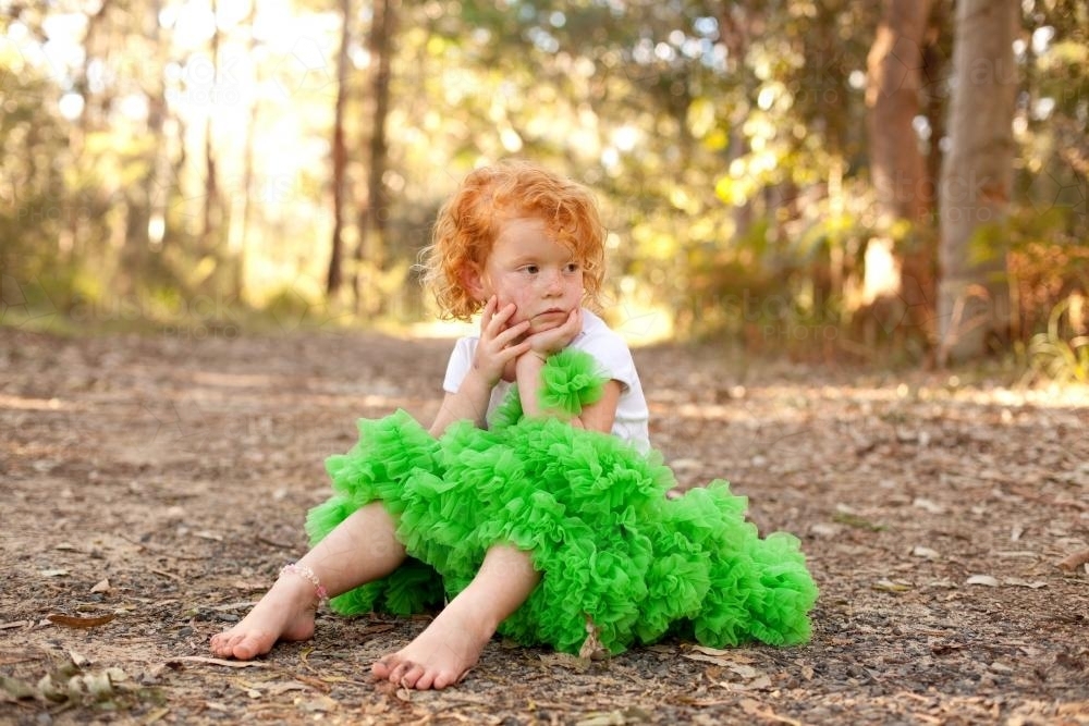 Young girl sitting on a track wearing a green tutu skirt - Australian Stock Image