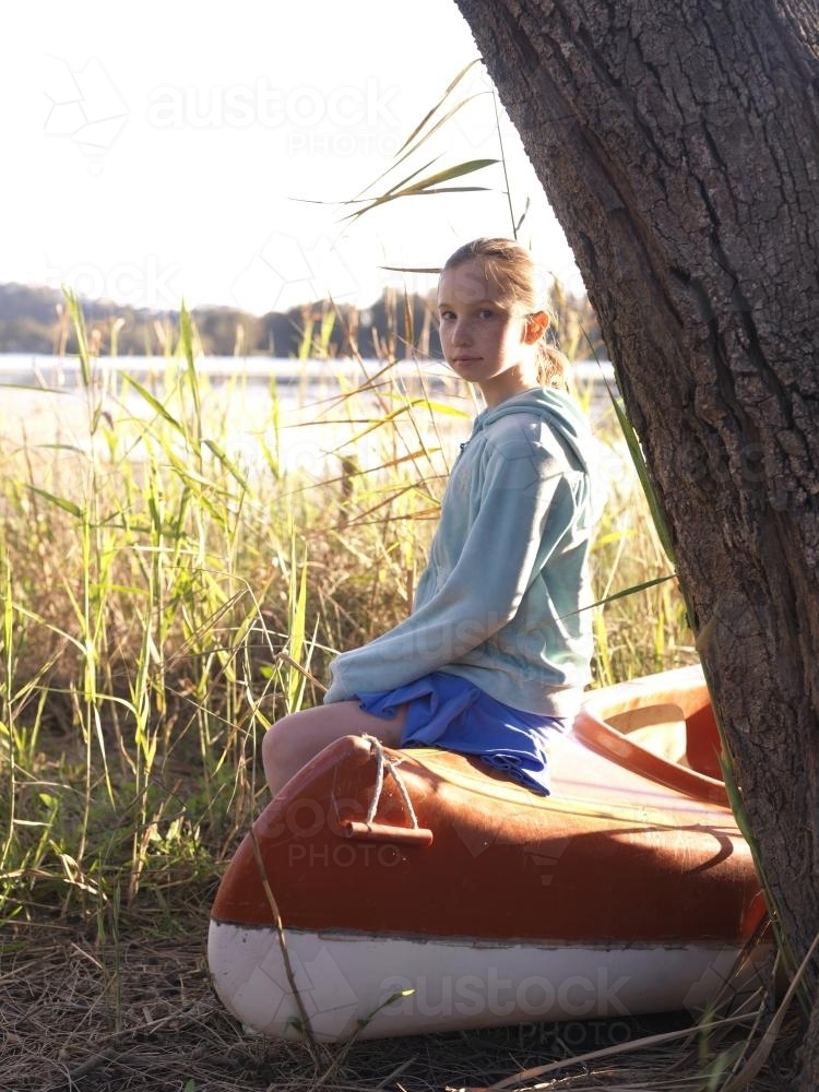 Young girl sitting on canoe beside a lake - Australian Stock Image