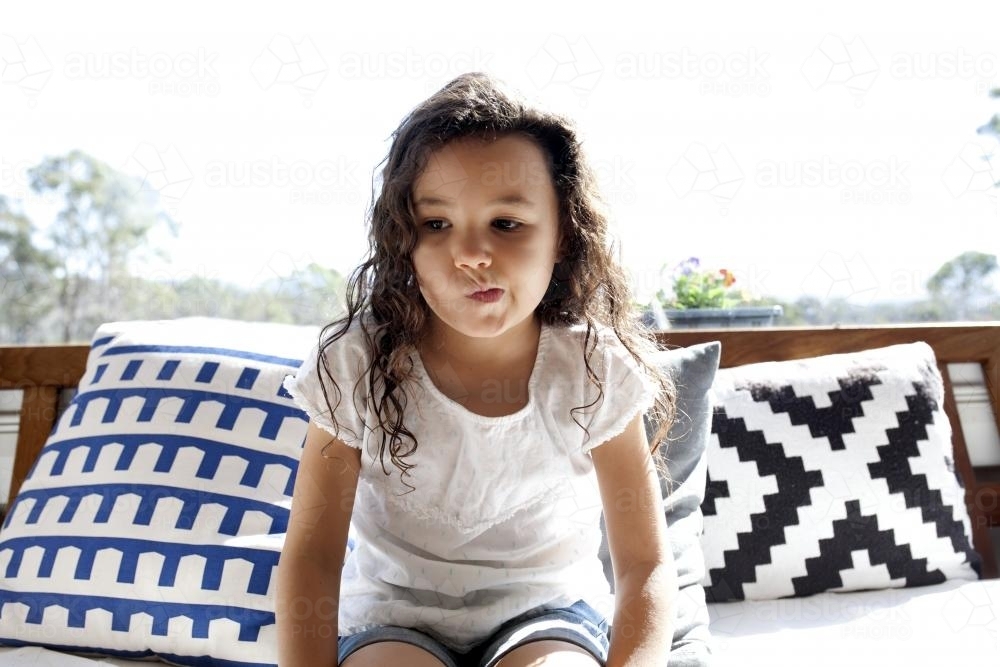 Young girl sitting on couch with cushions - Australian Stock Image