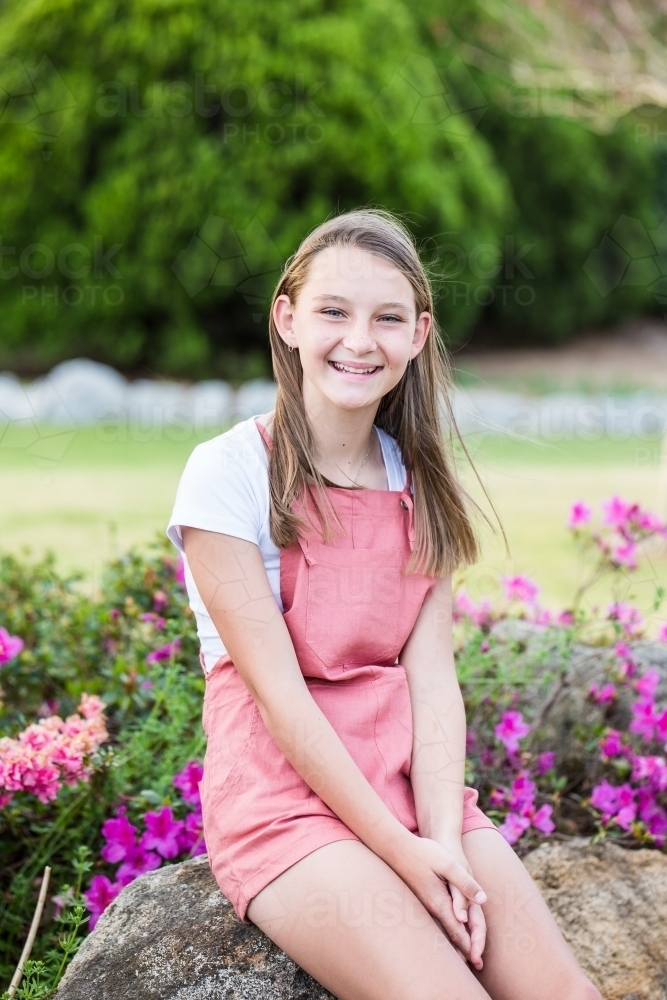 Young girl sitting on rock in garden smiling happy - Australian Stock Image
