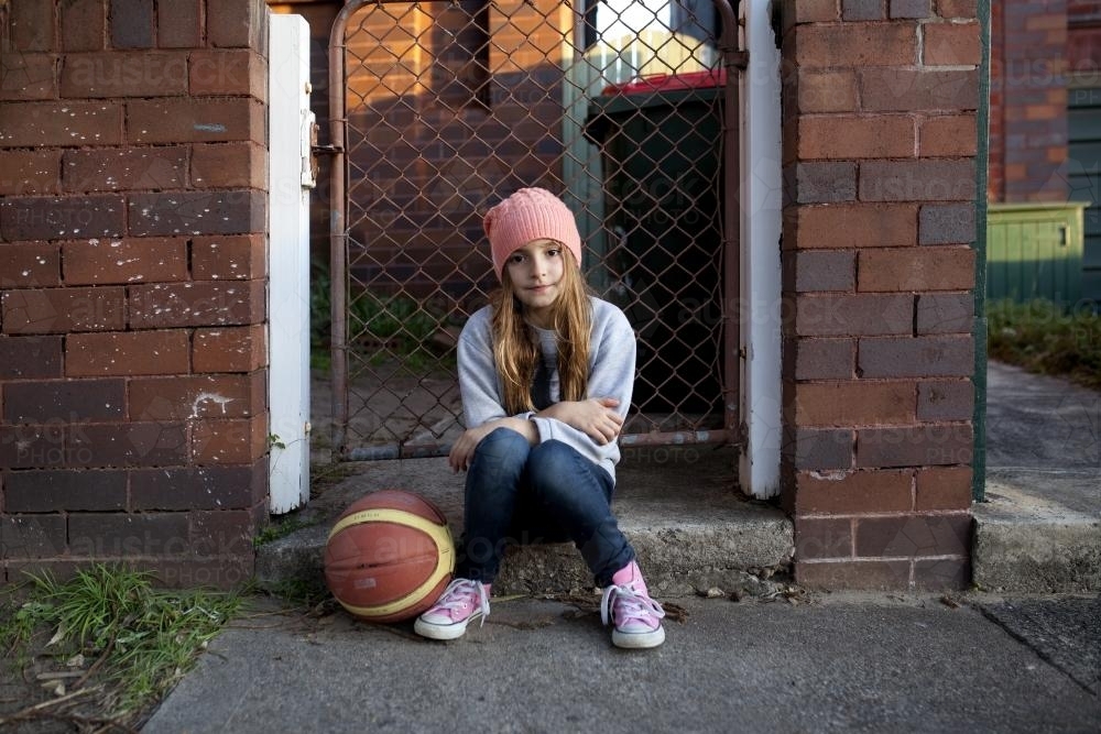 Young girl sitting on sidewalk with basketball - Australian Stock Image