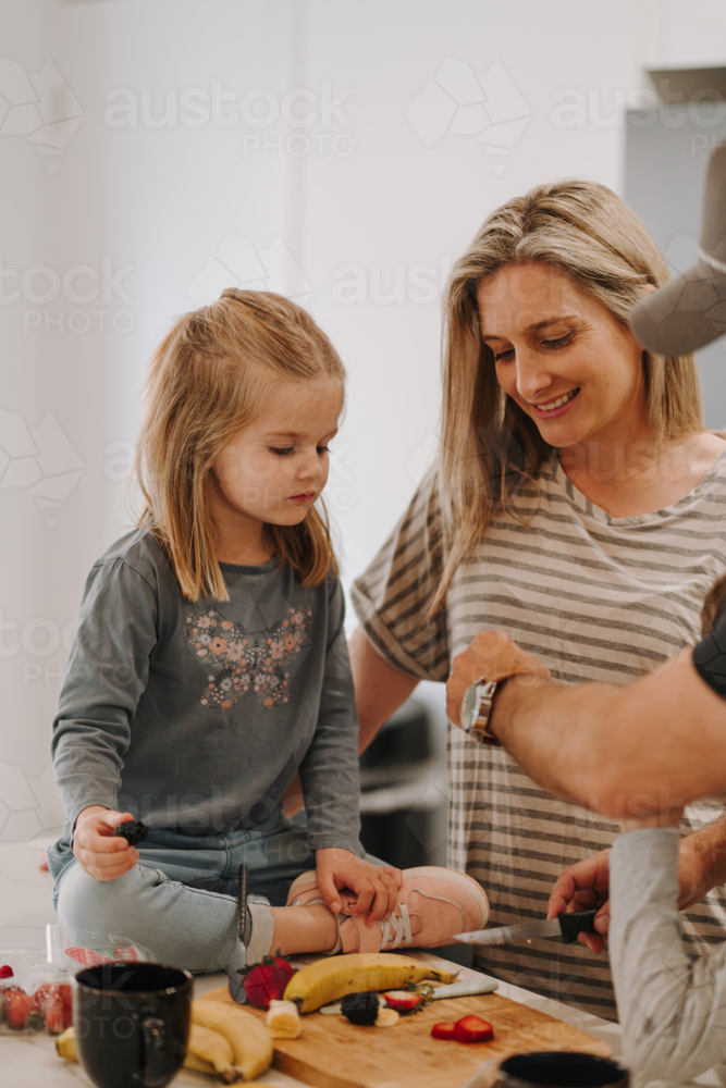 Young girl sitting on the countertop while preparing food. - Australian Stock Image