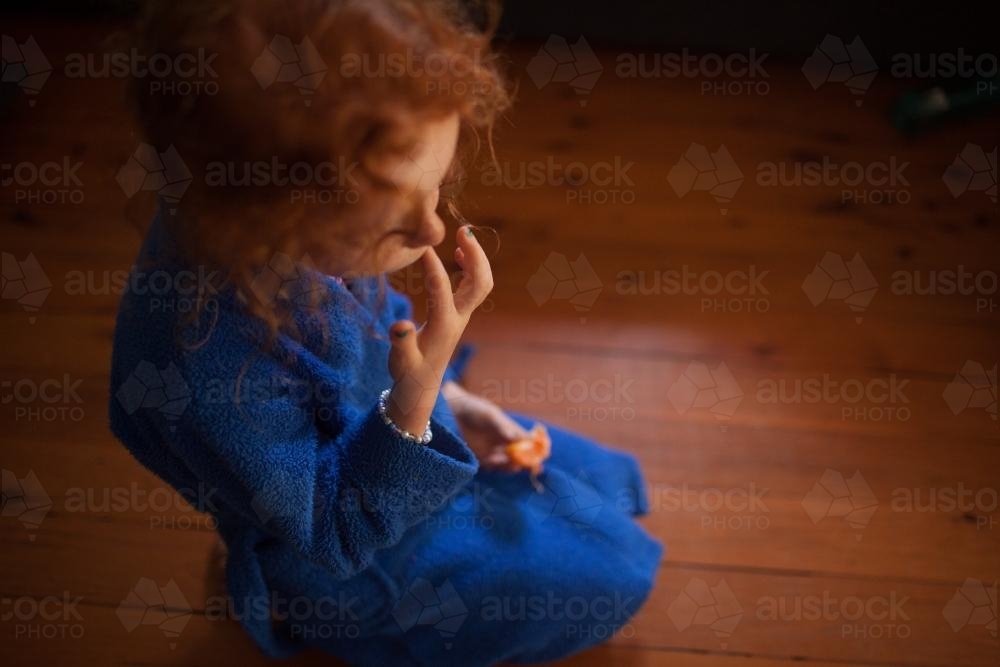 Young girl sitting on the floor eating a mandarin - Australian Stock Image