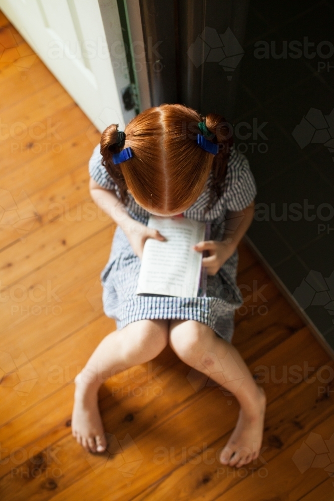 Young girl sitting on the floor reading a book - Australian Stock Image