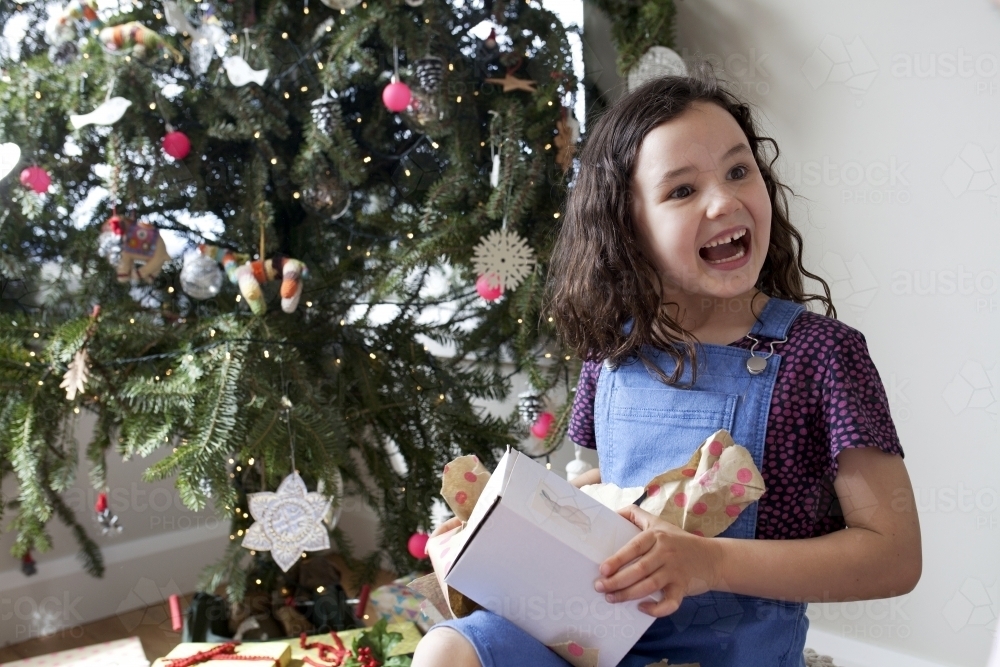 Young girl smiling and happy after opening Christmas present - Australian Stock Image