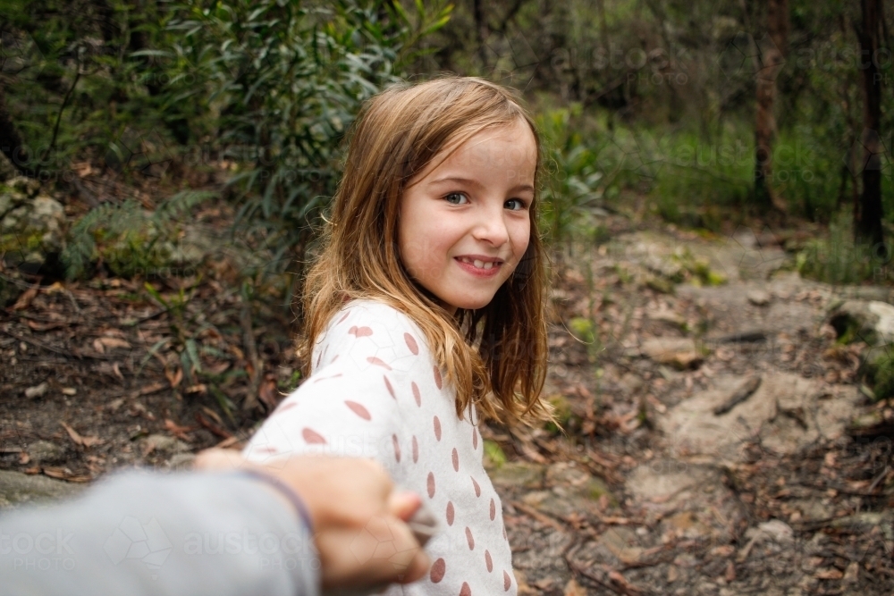 Young girl smiling in the wilderness holding parents hand on an adventure - Australian Stock Image