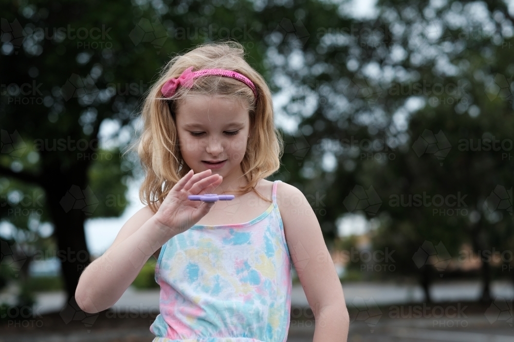 Young girl smiling playing with fidget spinner toy - Australian Stock Image