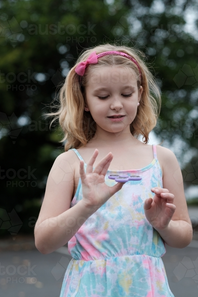Young girl smiling playing with fidget spinner toy - Australian Stock Image