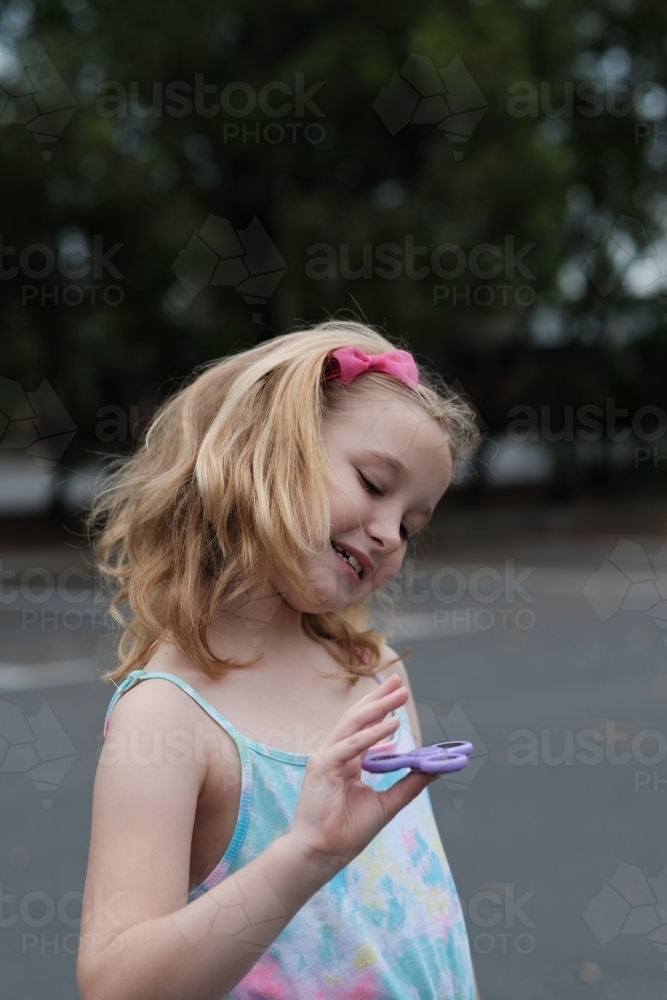 Young girl smiling playing with fidget spinner toy - Australian Stock Image