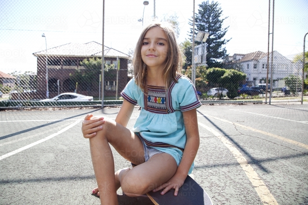 Young girl smiling sitting on skateboard - Australian Stock Image