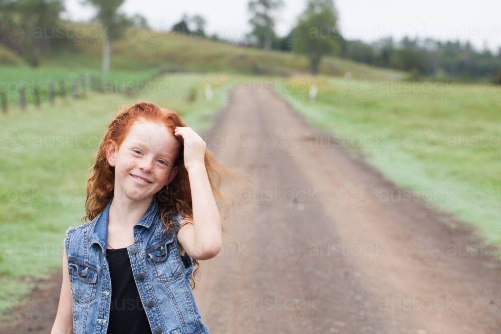 Young girl smiling while standing on a dirt road - Australian Stock Image