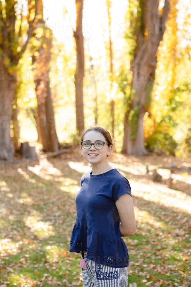 Young girl smiling with autumn trees behind her - Australian Stock Image