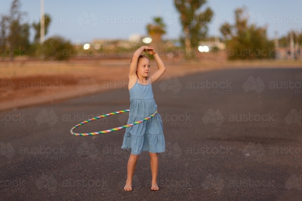 young girl spinning hula hoop around waist outside at duskq - Australian Stock Image