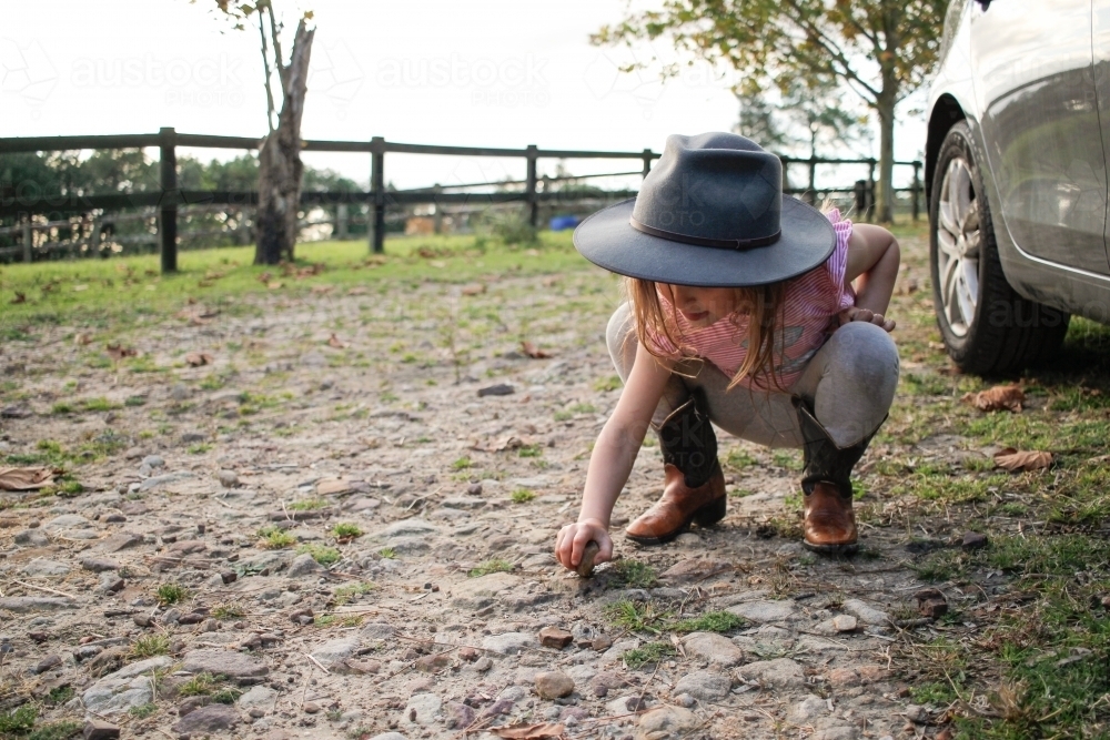 Young girl squatting examining stones in rocky rural ground - Australian Stock Image