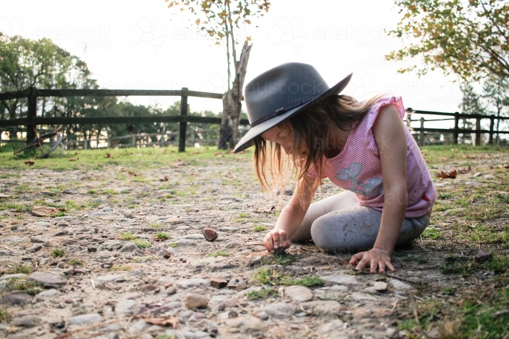 Young girl squatting examining stones in rocky rural ground - Australian Stock Image