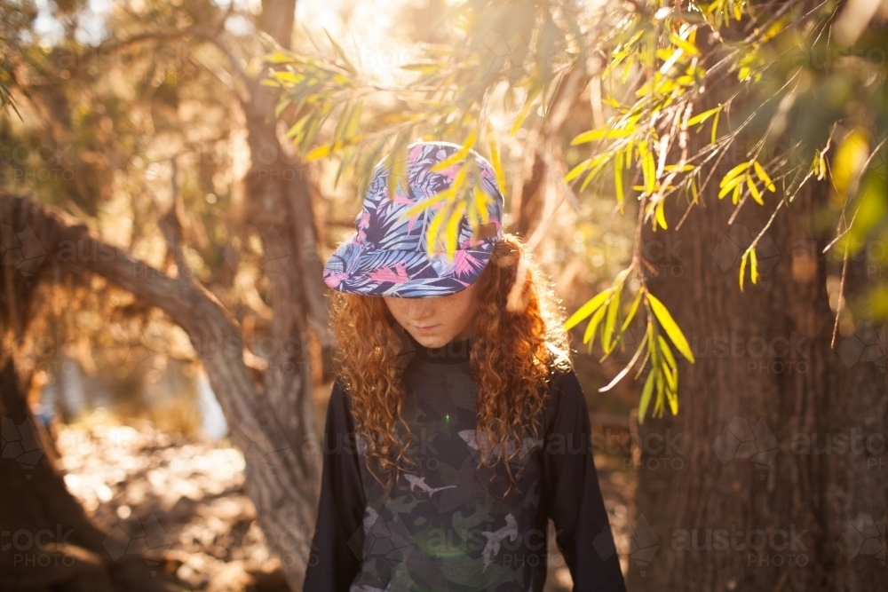 Young girl standing among trees in afternoon light - Australian Stock Image