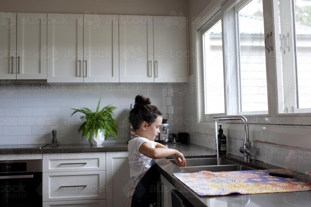 Young girl standing at sink in kitchen - Australian Stock Image