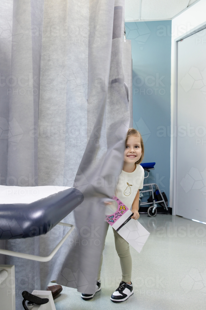 Young girl standing behind curtains holding a notebook - Australian Stock Image