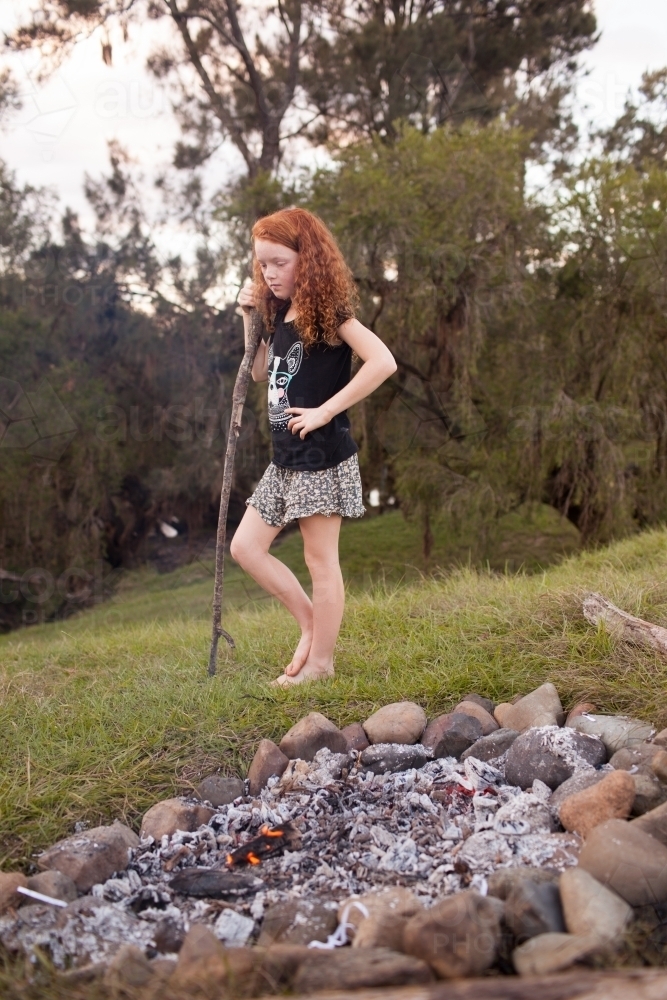 Young girl standing beside a campfire - Australian Stock Image