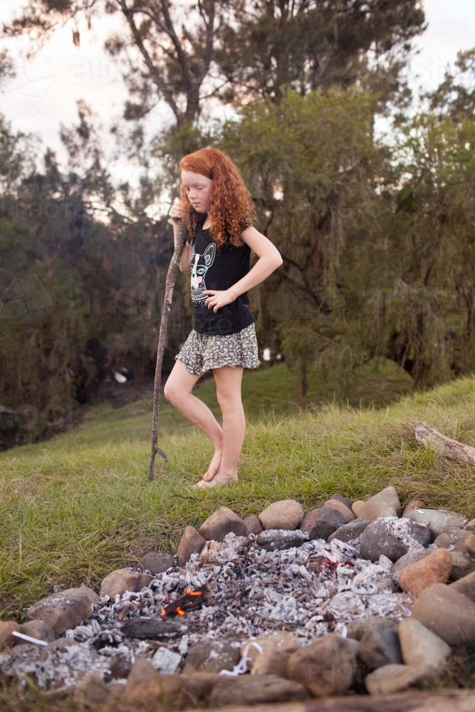 Young girl standing beside a campfire - Australian Stock Image